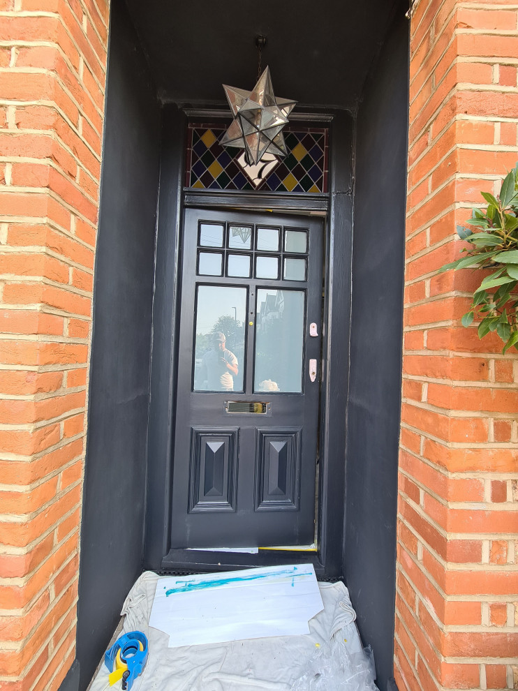 Mid-sized traditional front door in London with black walls, dark hardwood floors, a single front door, a black front door, brown floor and recessed.