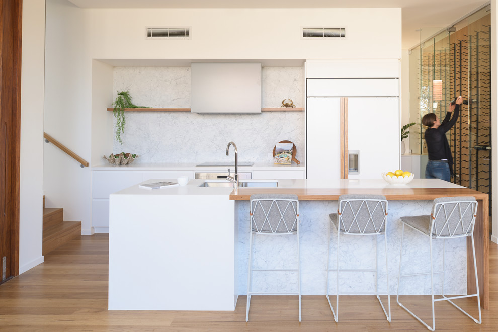 Contemporary galley kitchen in Brisbane with an undermount sink, flat-panel cabinets, white cabinets, medium hardwood floors, with island, brown floor and white benchtop.