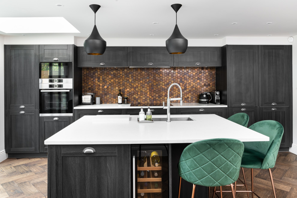 Design ideas for a large transitional single-wall eat-in kitchen in London with a drop-in sink, recessed-panel cabinets, black cabinets, quartzite benchtops, metallic splashback, metal splashback, stainless steel appliances, light hardwood floors, with island, brown floor and white benchtop.