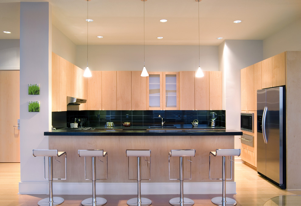 Photo of a mid-sized modern u-shaped eat-in kitchen in Seattle with light hardwood floors, flat-panel cabinets, light wood cabinets, granite benchtops, black splashback, ceramic splashback, stainless steel appliances and a peninsula.