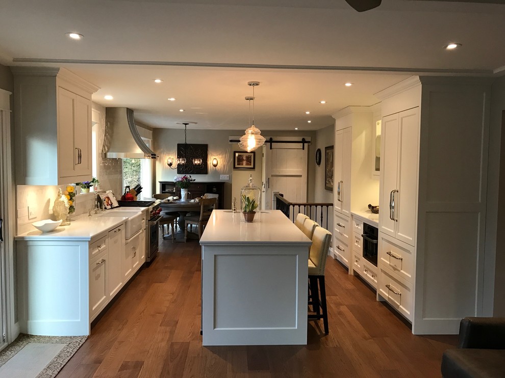 Large traditional galley eat-in kitchen in Toronto with a farmhouse sink, shaker cabinets, white cabinets, quartzite benchtops, panelled appliances, medium hardwood floors and with island.