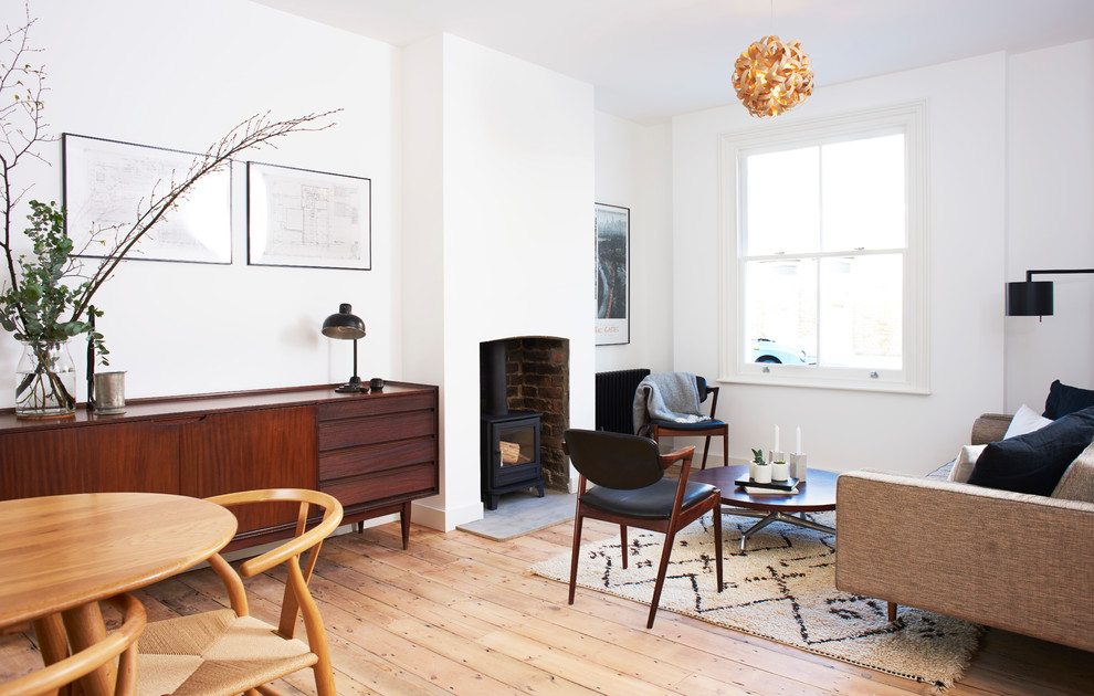 Photo of a mid-sized midcentury open concept family room in London with white walls, medium hardwood floors, a wood stove and a brick fireplace surround.