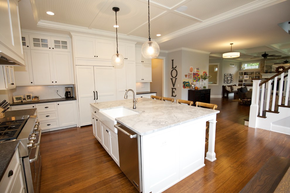 This is an example of a large country u-shaped eat-in kitchen in Chicago with a farmhouse sink, shaker cabinets, white cabinets, quartzite benchtops, white splashback, subway tile splashback, stainless steel appliances, medium hardwood floors, with island, brown floor and white benchtop.