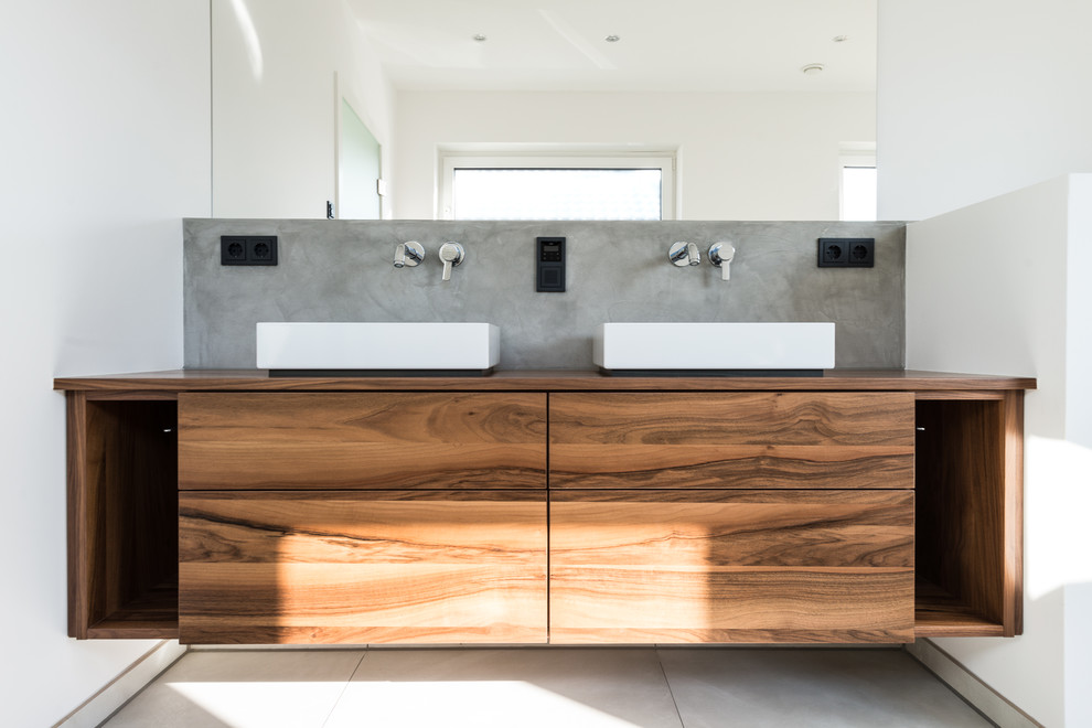 Design ideas for a mid-sized contemporary 3/4 bathroom in Dusseldorf with flat-panel cabinets, dark wood cabinets, a drop-in tub, a curbless shower, a wall-mount toilet, gray tile, cement tile, white walls, ceramic floors, a vessel sink and wood benchtops.