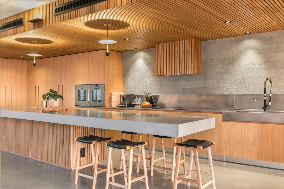 Expansive industrial l-shaped open plan kitchen in Perth with a single-bowl sink, solid surface benchtops, grey splashback, matchstick tile splashback, stainless steel appliances, ceramic floors, grey floor, grey benchtop, flat-panel cabinets, light wood cabinets, with island and wood.