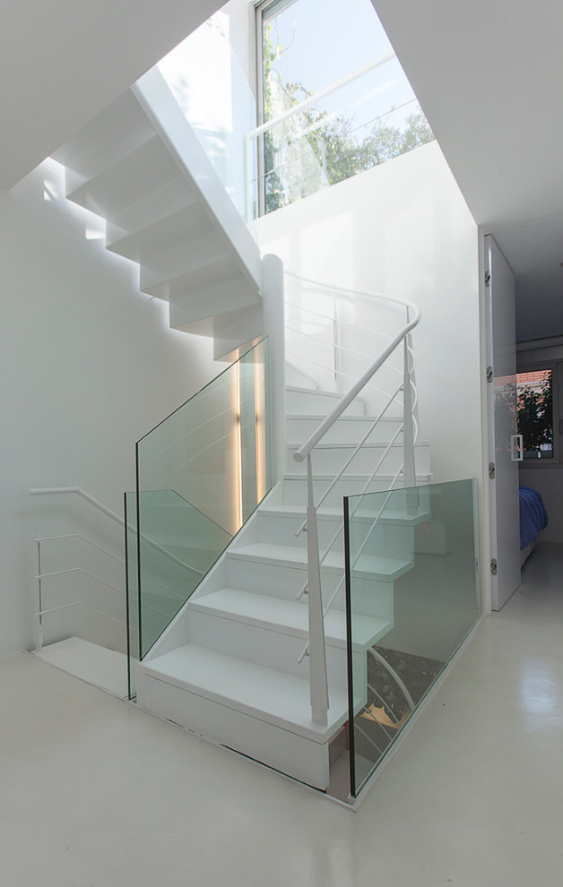 This is an example of a large contemporary painted wood curved staircase in Barcelona with painted wood risers and metal railing.