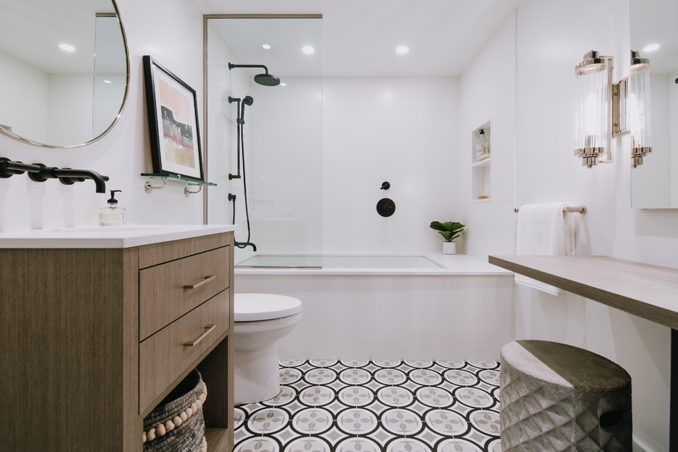 Photo of a mid-sized contemporary 3/4 bathroom in Montreal with flat-panel cabinets, medium wood cabinets, an undermount tub, a shower/bathtub combo, a two-piece toilet, white tile, ceramic tile, white walls, porcelain floors, an undermount sink, engineered quartz benchtops, grey floor, an open shower and white benchtops.