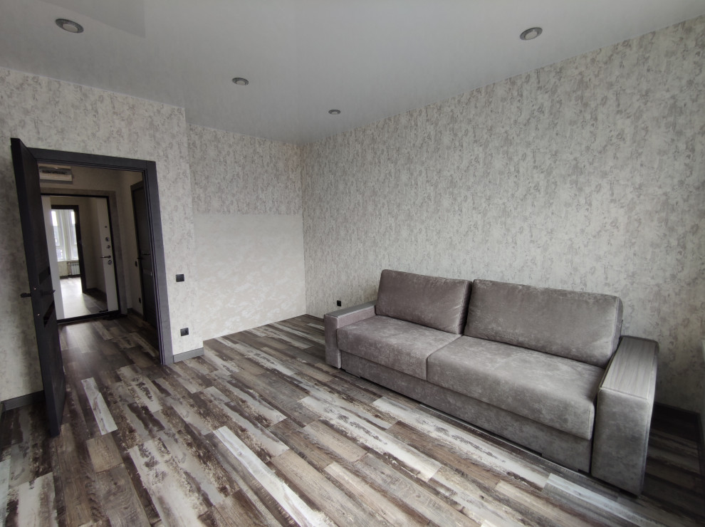 На фото: большая гостиная комната с серыми стенами, полом из винила, обоями на стенах, коричневым полом и коричневым диваном с