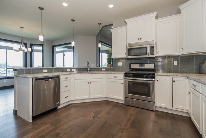 Example of a large transitional u-shaped light wood floor and brown floor eat-in kitchen design in Cedar Rapids with an undermount sink, shaker cabinets, white cabinets, quartz countertops, green backsplash, glass tile backsplash, stainless steel appliances and no island