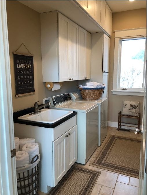 Design ideas for a mid-sized transitional galley dedicated laundry room in Minneapolis with an utility sink, recessed-panel cabinets, white cabinets, laminate benchtops, beige walls, porcelain floors, a side-by-side washer and dryer, beige floor and black benchtop.