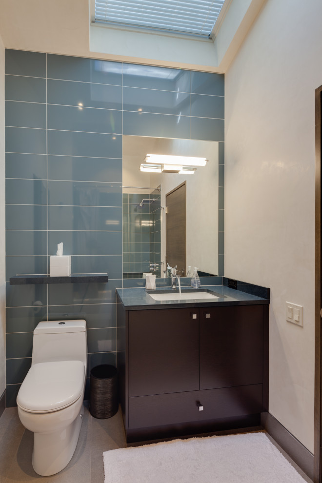 This is an example of a small modern kids bathroom in Denver with flat-panel cabinets, brown cabinets, an undermount tub, a shower/bathtub combo, a one-piece toilet, blue tile, porcelain tile, white walls, porcelain floors, an undermount sink, engineered quartz benchtops, grey floor, a hinged shower door, brown benchtops, a single vanity and a built-in vanity.