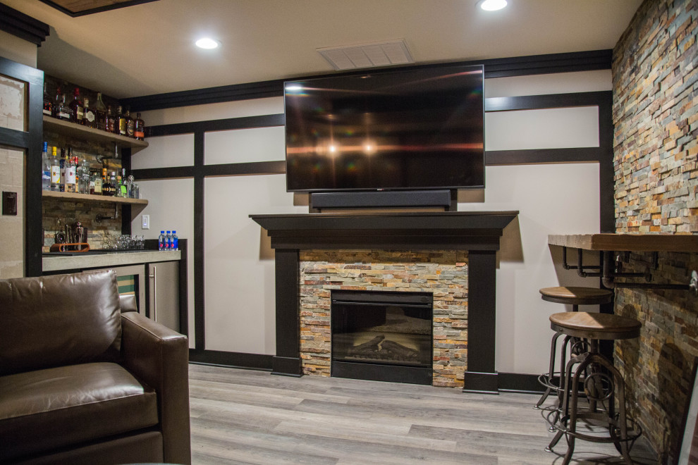 This is an example of a large contemporary fully buried basement in Indianapolis with a home bar, brown walls, laminate floors, a standard fireplace, a stacked stone fireplace surround, brown floors and brick walls.