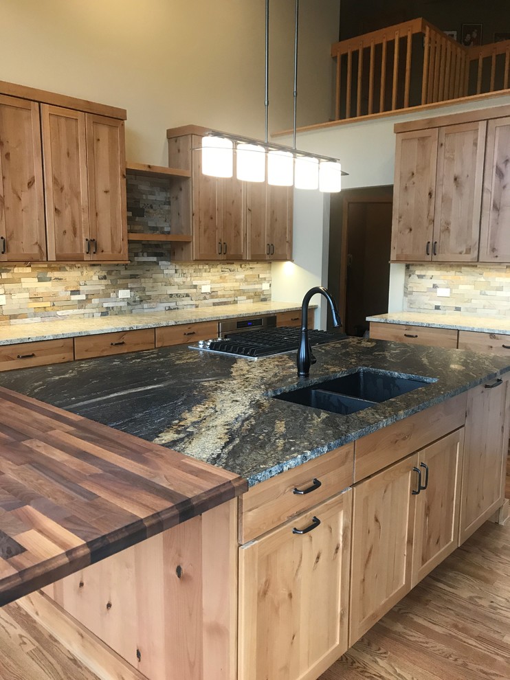 Photo of a large country l-shaped open plan kitchen in Chicago with an undermount sink, shaker cabinets, medium wood cabinets, granite benchtops, green splashback, slate splashback, stainless steel appliances, medium hardwood floors, with island, brown floor and black benchtop.