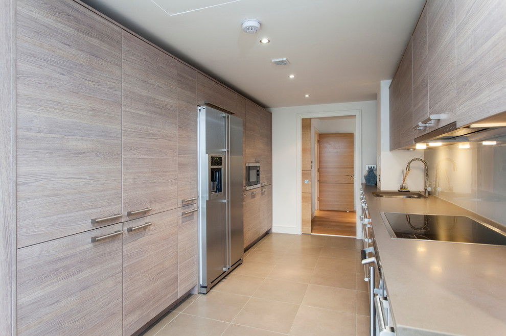 Inspiration for a contemporary galley separate kitchen in London with flat-panel cabinets, grey cabinets, grey splashback, glass sheet splashback and stainless steel appliances.