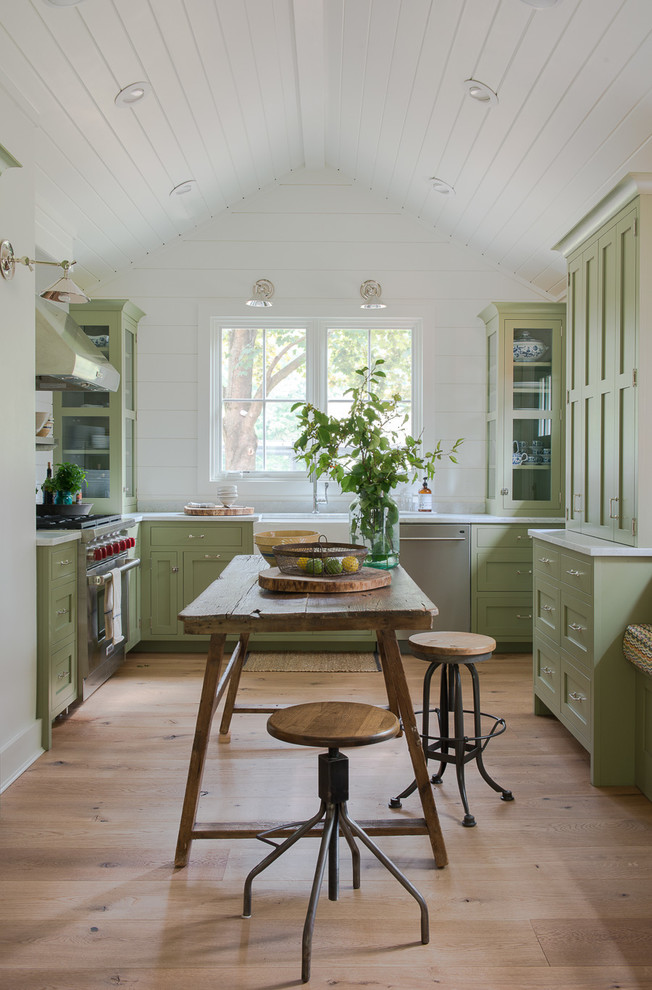 This is an example of a country kitchen in New York with a farmhouse sink, shaker cabinets, green cabinets, stainless steel appliances, light hardwood floors and no island.