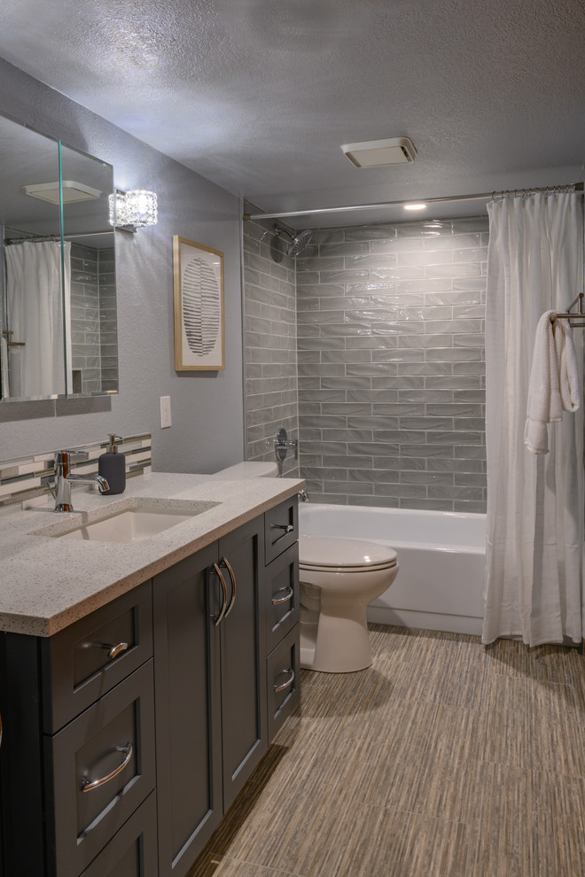 This is an example of a mid-sized transitional master bathroom in Denver with shaker cabinets, blue cabinets, grey walls, porcelain floors, an undermount sink, engineered quartz benchtops, brown floor, grey benchtops, an alcove tub, a shower/bathtub combo, gray tile, subway tile and a shower curtain.