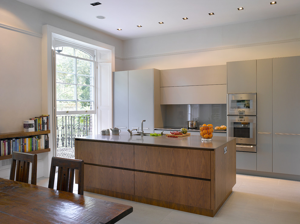 Inspiration for a large contemporary galley eat-in kitchen in London with flat-panel cabinets, grey cabinets, solid surface benchtops, grey splashback, glass sheet splashback, stainless steel appliances, with island, beige floor, brown benchtop and an undermount sink.
