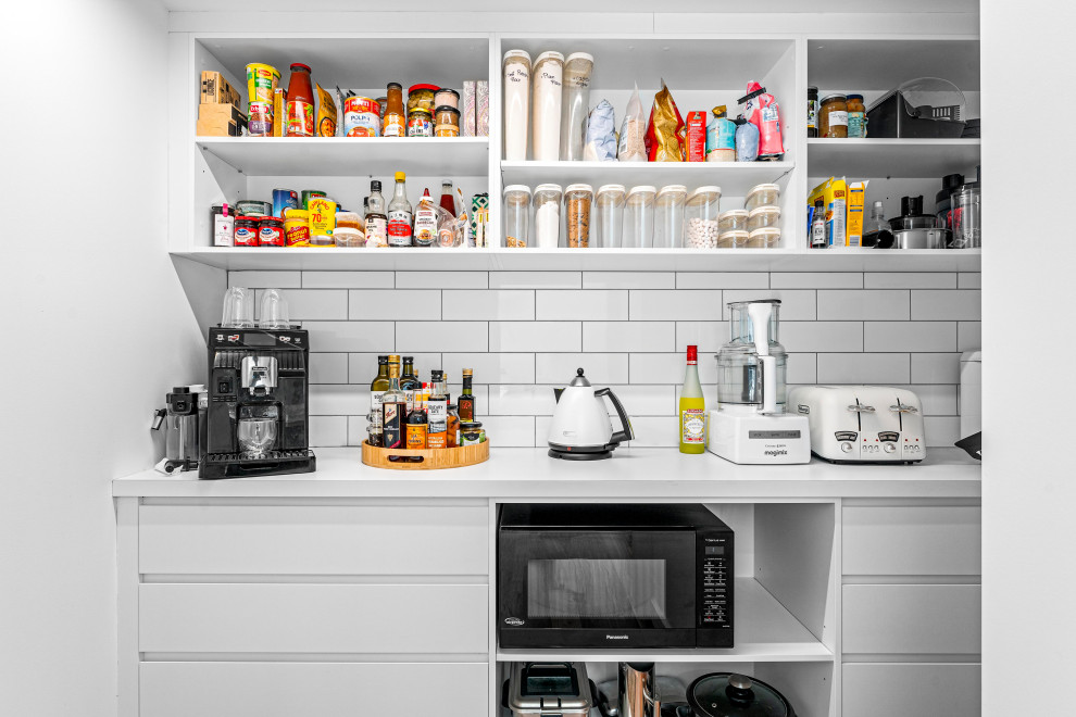 Photo of a modern single-wall kitchen pantry in Central Coast with flat-panel cabinets, white splashback, black appliances, medium hardwood floors, brown floor and white benchtop.