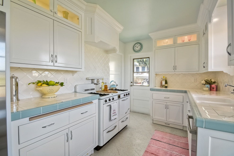 Mid-sized transitional galley separate kitchen in San Diego with a double-bowl sink, recessed-panel cabinets, white cabinets, tile benchtops, white splashback, ceramic splashback, white appliances, terrazzo floors and no island.