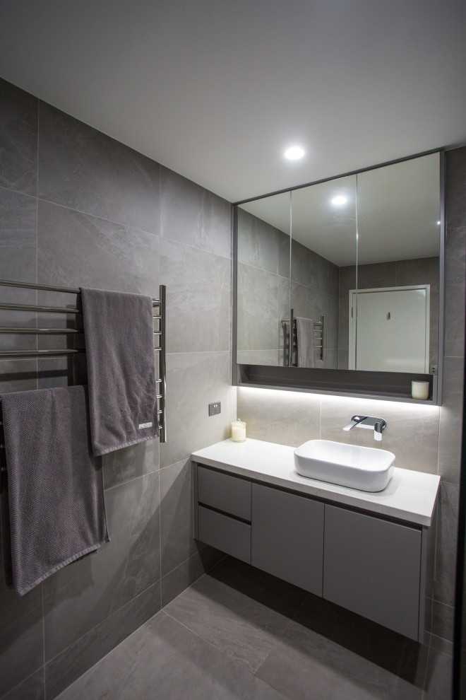 Mid-sized modern kids bathroom in Brisbane with flat-panel cabinets, grey cabinets, a corner shower, gray tile, porcelain tile, grey walls, porcelain floors, a vessel sink, engineered quartz benchtops, grey floor, a hinged shower door, white benchtops and a two-piece toilet.