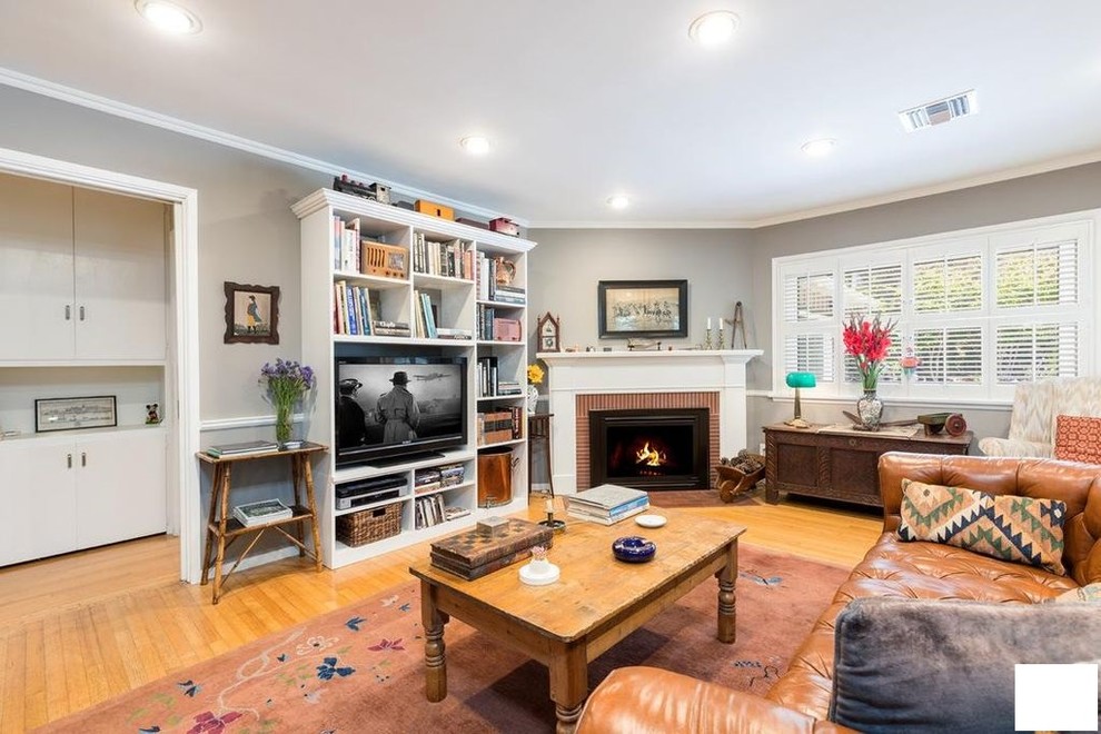 Photo of a large country open concept family room in Los Angeles with a library, grey walls, medium hardwood floors, a wood stove, a brick fireplace surround, a built-in media wall and brown floor.