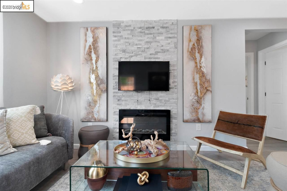 This is an example of a mid-sized modern open concept living room in San Francisco with grey walls, light hardwood floors, grey floor, a standard fireplace and a wall-mounted tv.