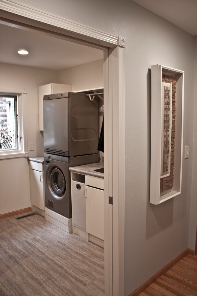 Inspiration for a small transitional u-shaped laundry cupboard in Other with an integrated sink, flat-panel cabinets, white cabinets, laminate benchtops, grey walls, vinyl floors and a stacked washer and dryer.