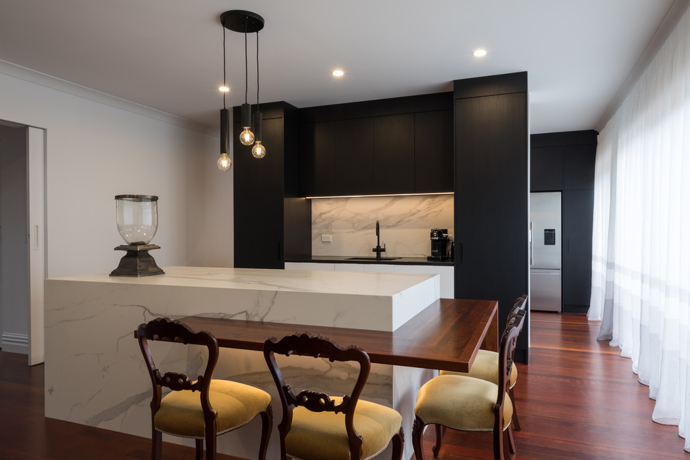 Photo of a contemporary galley kitchen in Other with an integrated sink, flat-panel cabinets, black cabinets, white splashback, stone slab splashback, medium hardwood floors, with island, brown floor and white benchtop.