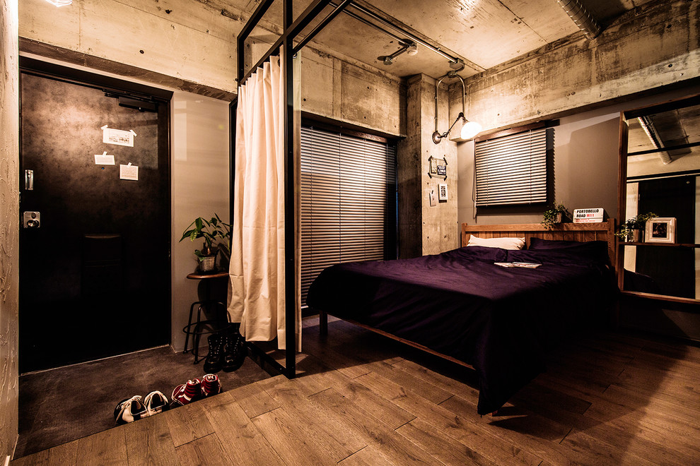 Photo of an industrial bedroom with grey walls, medium hardwood floors and brown floor.
