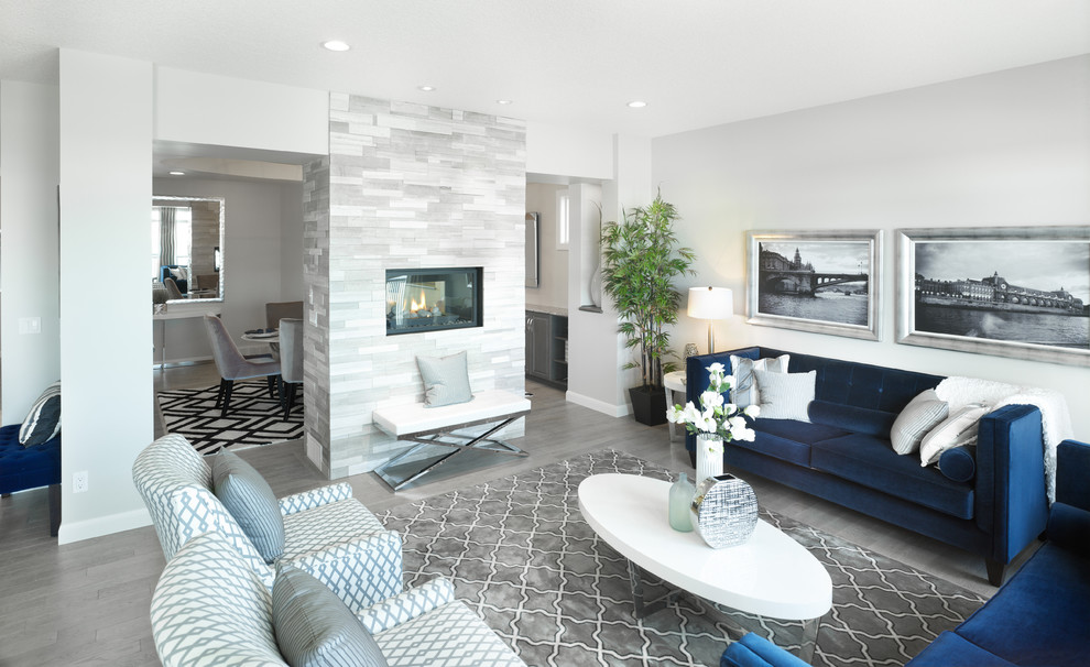 This is an example of a mid-sized transitional formal open concept living room in Calgary with grey walls, medium hardwood floors, a two-sided fireplace, a tile fireplace surround and no tv.