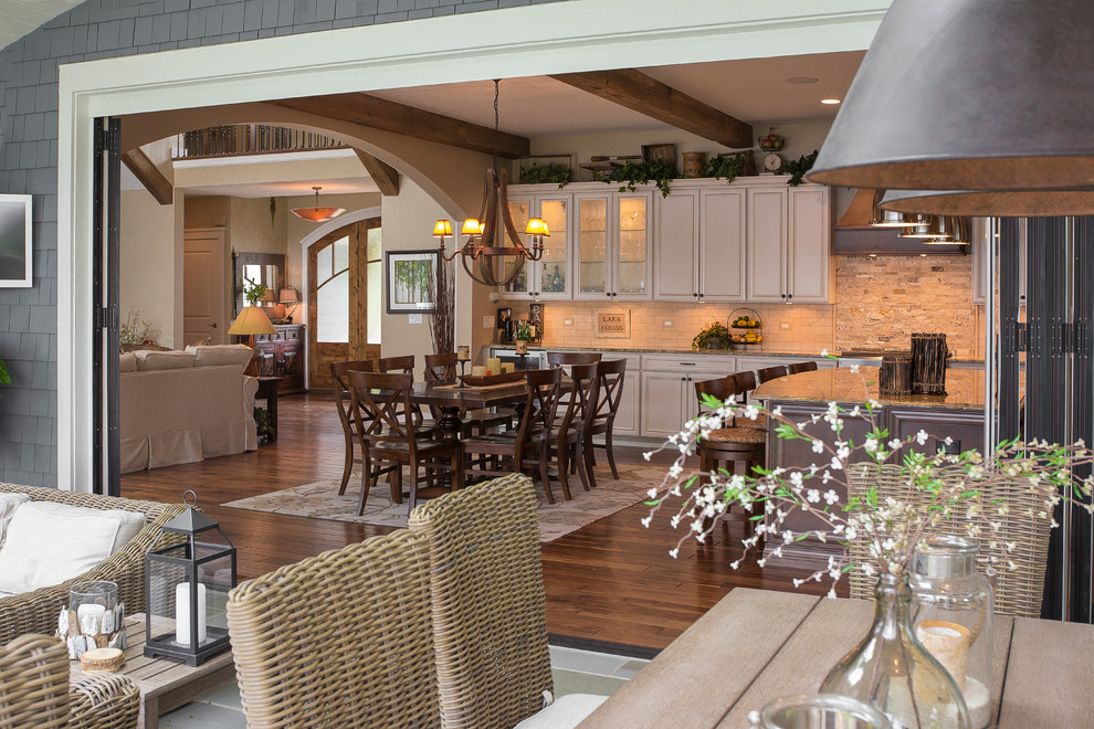 Large transitional l-shaped medium tone wood floor eat-in kitchen photo in Milwaukee with a farmhouse sink, raised-panel cabinets, white cabinets, granite countertops, multicolored backsplash, stone tile backsplash, stainless steel appliances and an island