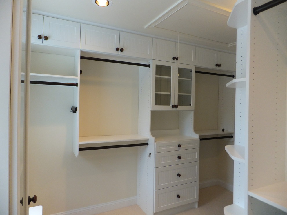 Photo of a mid-sized beach style gender-neutral dressing room in Manchester with glass-front cabinets, white cabinets and carpet.