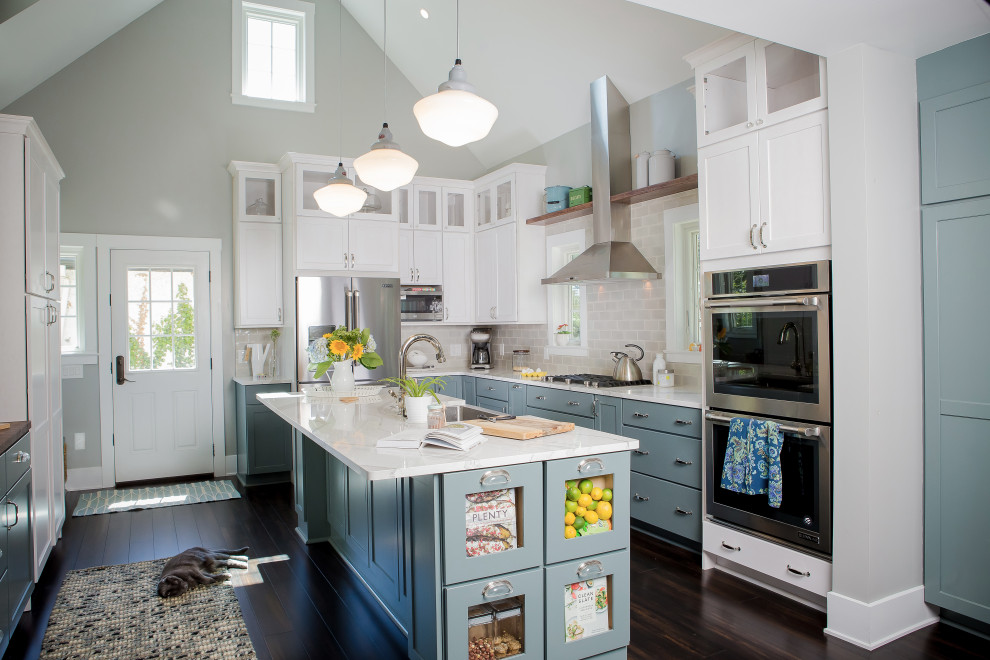 This is an example of a transitional u-shaped kitchen in Other with a farmhouse sink, shaker cabinets, blue cabinets, grey splashback, subway tile splashback, dark hardwood floors, with island, brown floor, white benchtop and vaulted.