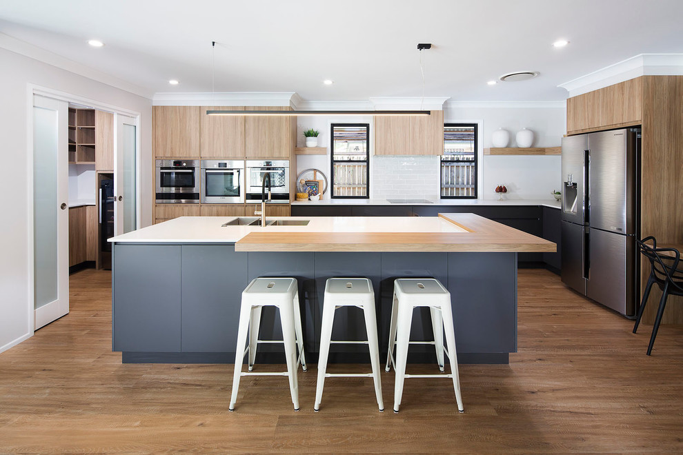 Design ideas for a contemporary l-shaped eat-in kitchen in Brisbane with an undermount sink, flat-panel cabinets, medium wood cabinets, white splashback, ceramic splashback, stainless steel appliances, medium hardwood floors, with island, brown floor and white benchtop.