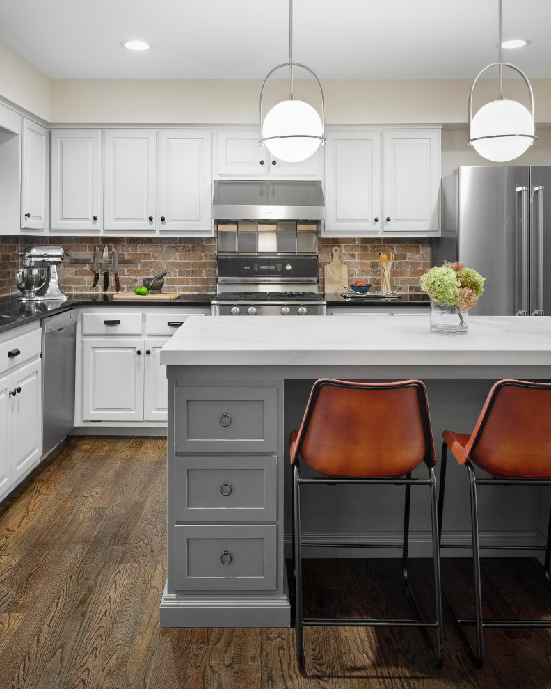 This is an example of a mid-sized midcentury l-shaped eat-in kitchen in New York with an undermount sink, raised-panel cabinets, grey cabinets, quartz benchtops, brown splashback, brick splashback, stainless steel appliances, dark hardwood floors, with island, brown floor and white benchtop.