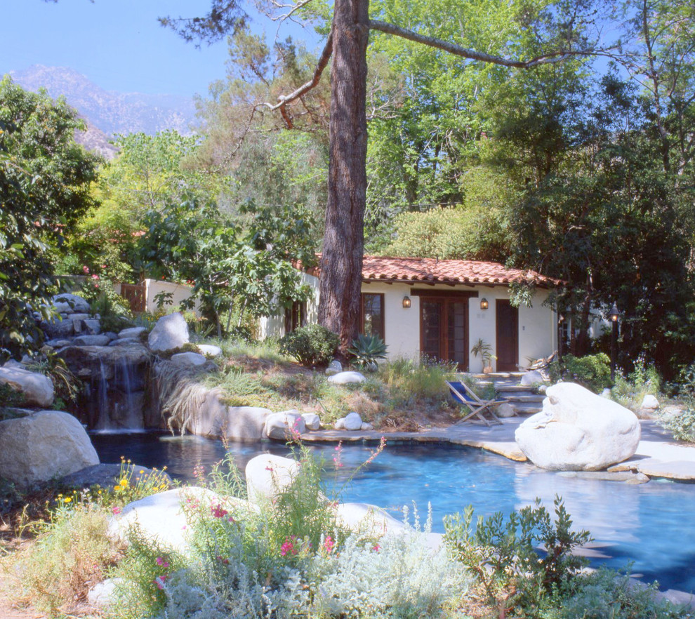 Design ideas for a mid-sized mediterranean backyard custom-shaped natural pool in Los Angeles with a pool house and natural stone pavers.
