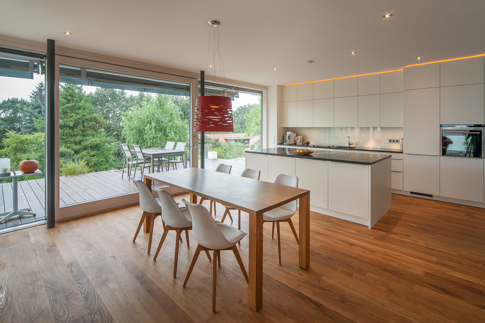 Design ideas for a large contemporary galley eat-in kitchen in Dresden with an undermount sink, flat-panel cabinets, white cabinets, white splashback, glass sheet splashback, medium hardwood floors, with island and panelled appliances.