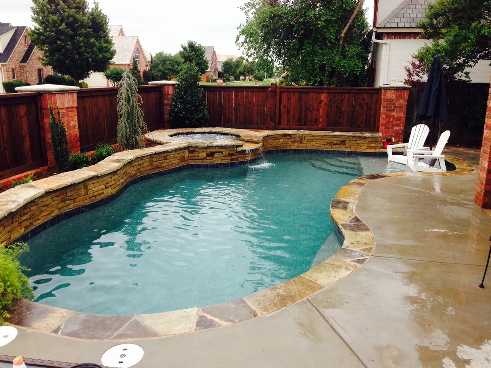 Photo of a mid-sized traditional side yard kidney-shaped natural pool in Oklahoma City with a water feature and stamped concrete.