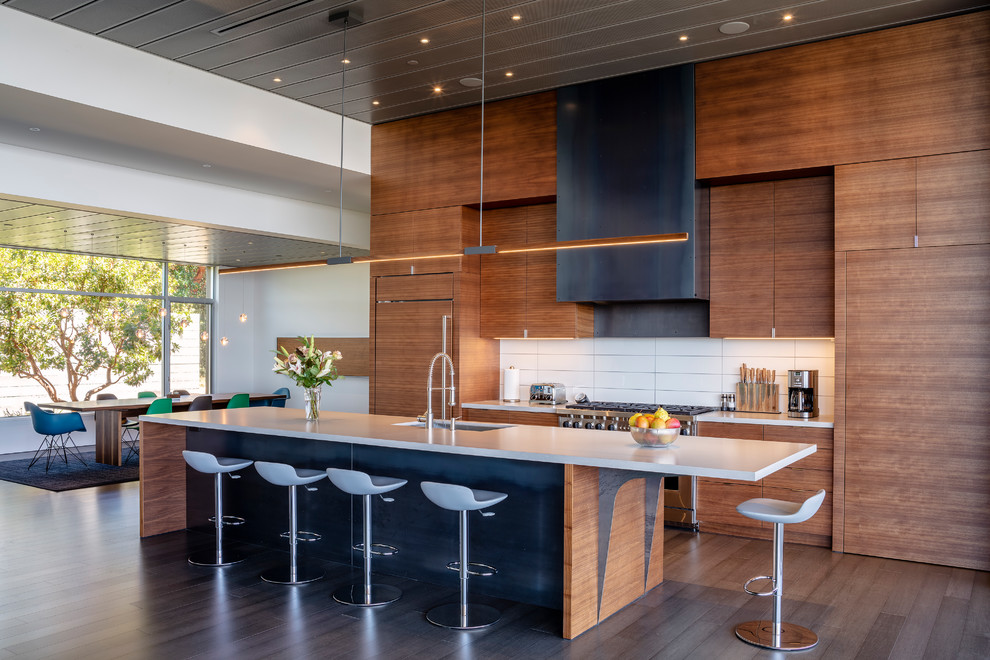 This is an example of a contemporary galley eat-in kitchen in San Francisco with an undermount sink, flat-panel cabinets, medium wood cabinets, white splashback, panelled appliances, with island, brown floor and white benchtop.