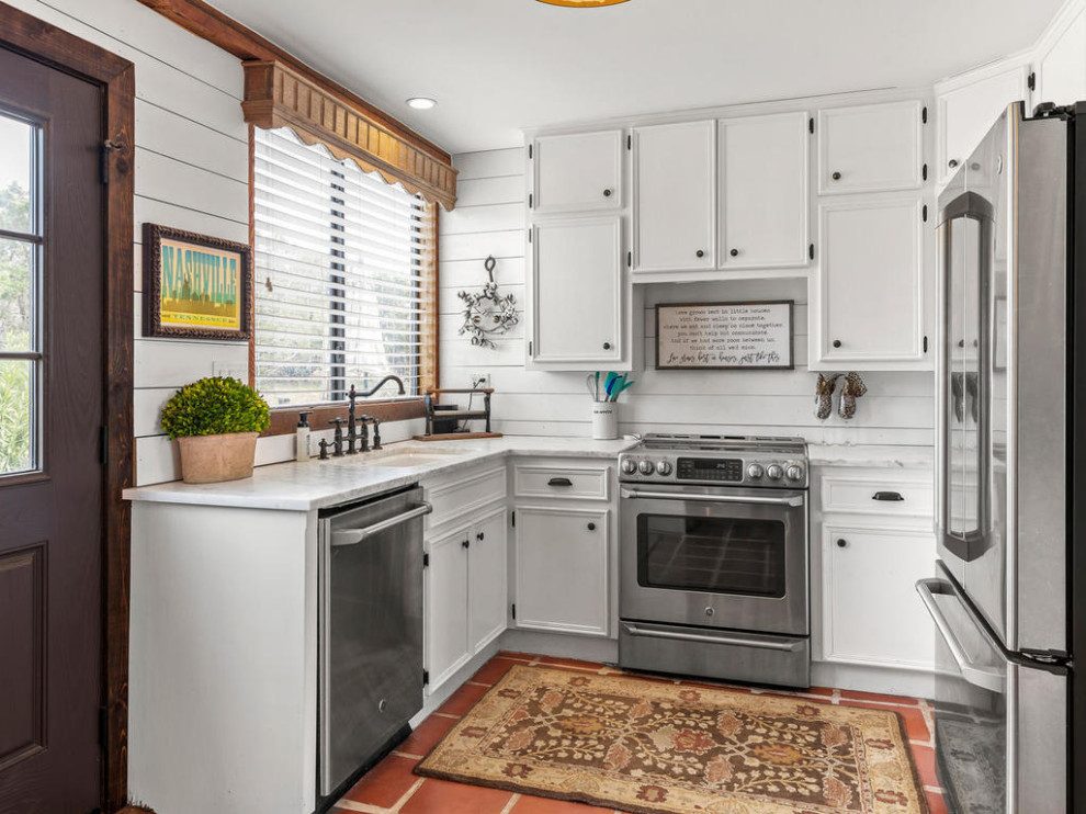 Inspiration for a country u-shaped kitchen in Austin with an undermount sink, raised-panel cabinets, white cabinets, quartzite benchtops, white splashback, shiplap splashback, stainless steel appliances, terra-cotta floors, no island and white benchtop.