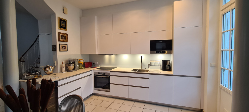 Exemple de cuisine ouverte in L With un évier intégré, un placard à porte plane, des portes de placard blanches, un plan de travail en surface solide, une crédence blanche, une crédence en dalle métallique, un électroménager en acier inoxydable, un sol en carrelage de céramique, aucun îlot, un sol blanc and un plan de travail beige.