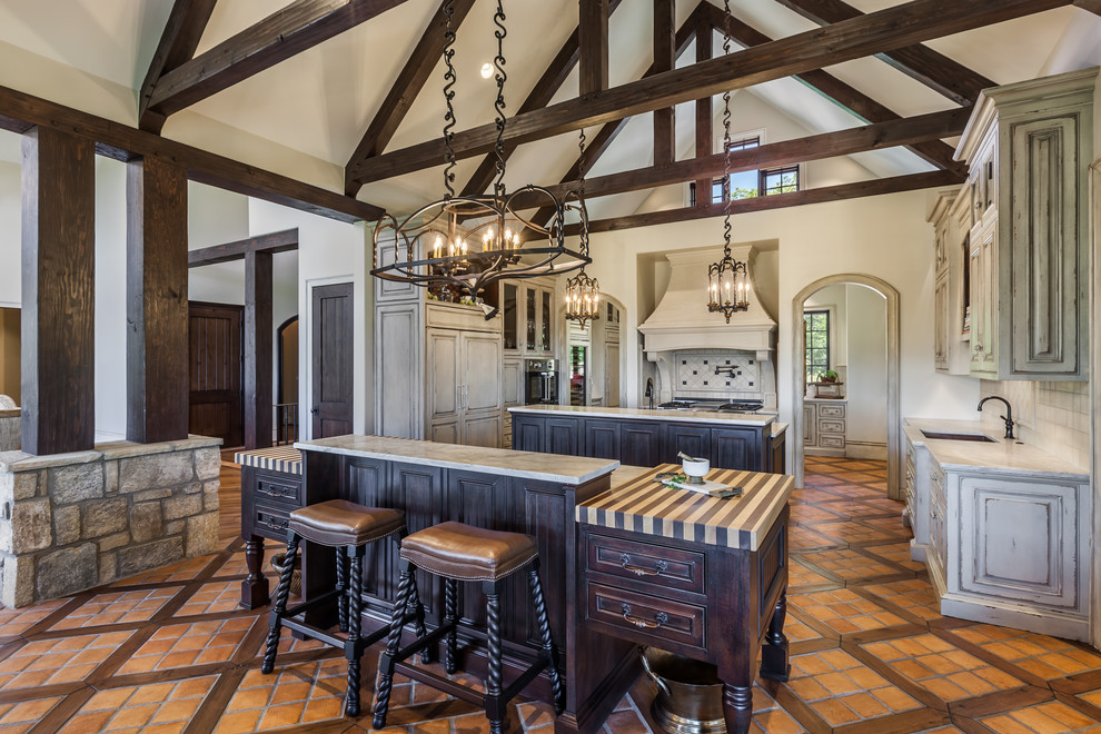 Inspiration for a rustic terra-cotta tile kitchen remodel with an undermount sink, raised-panel cabinets, distressed cabinets, two islands and paneled appliances