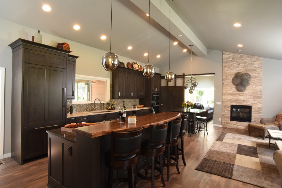 Open concept kitchen - mid-sized transitional galley medium tone wood floor and brown floor open concept kitchen idea in Seattle with an undermount sink, shaker cabinets, brown cabinets, wood countertops, metallic backsplash, glass sheet backsplash, paneled appliances and two islands