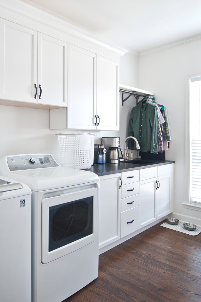 Inspiration for a large transitional galley dedicated laundry room in Nashville with an undermount sink, recessed-panel cabinets, white cabinets, granite benchtops, white walls, medium hardwood floors, a side-by-side washer and dryer, brown floor and black benchtop.