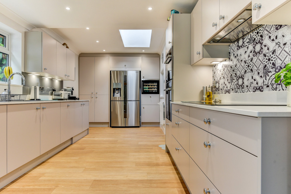 This is an example of a mid-sized contemporary galley eat-in kitchen in Sussex with an integrated sink, flat-panel cabinets, grey cabinets, quartzite benchtops, grey splashback, glass tile splashback, black appliances, medium hardwood floors, no island, brown floor and white benchtop.