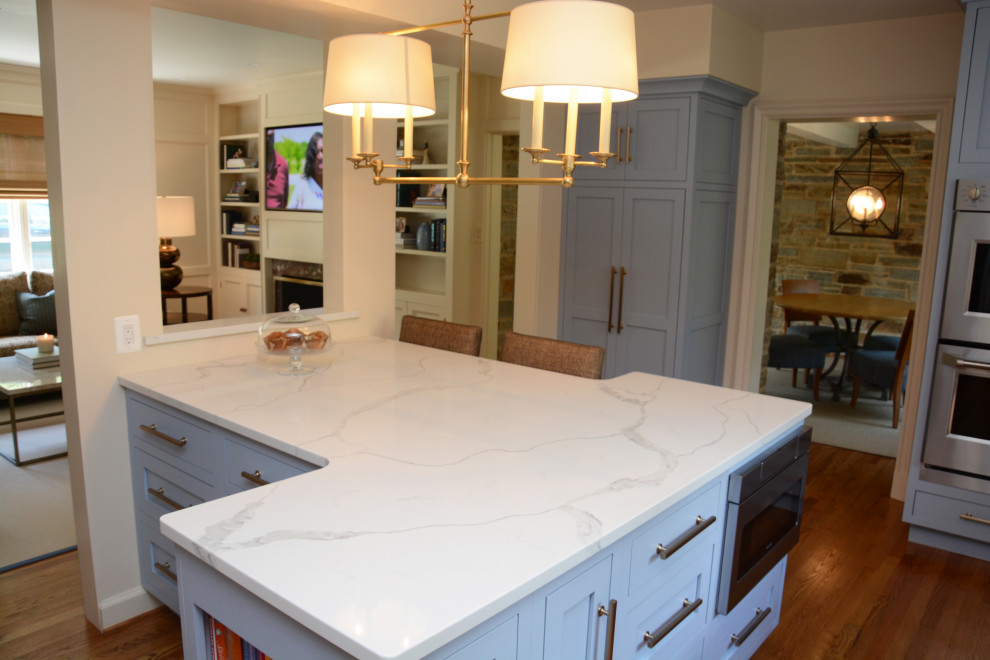 This is an example of a mid-sized transitional u-shaped separate kitchen in Baltimore with an undermount sink, shaker cabinets, blue cabinets, quartz benchtops, white splashback, engineered quartz splashback, stainless steel appliances, medium hardwood floors, with island, brown floor and white benchtop.