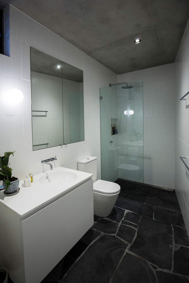 Mid-sized contemporary 3/4 bathroom in Sydney with flat-panel cabinets, white cabinets, an open shower, white tile, ceramic tile, white walls, cement tiles, an integrated sink, solid surface benchtops, grey floor and an open shower.