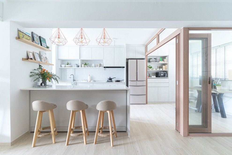 Inspiration for a contemporary galley kitchen in Singapore with flat-panel cabinets, white cabinets, white splashback, stainless steel appliances, light hardwood floors, a peninsula, beige floor and white benchtop.