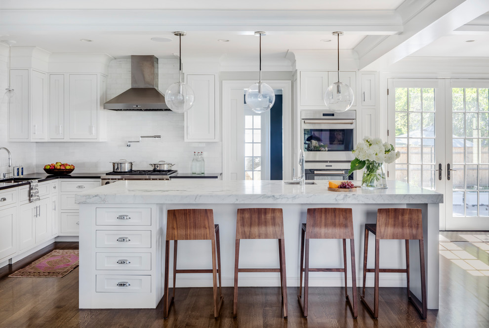 Design ideas for a large transitional l-shaped kitchen in Boston with a single-bowl sink, white cabinets, white splashback, stone tile splashback, stainless steel appliances, with island, brown floor, shaker cabinets, dark hardwood floors and marble benchtops.