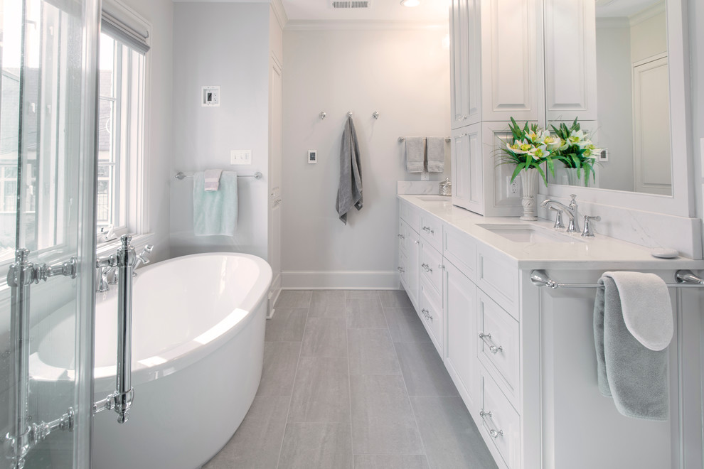 Design ideas for a large traditional master bathroom in Charlotte with raised-panel cabinets, white cabinets, a freestanding tub, white tile, white walls, porcelain floors, an undermount sink, engineered quartz benchtops, grey floor and white benchtops.